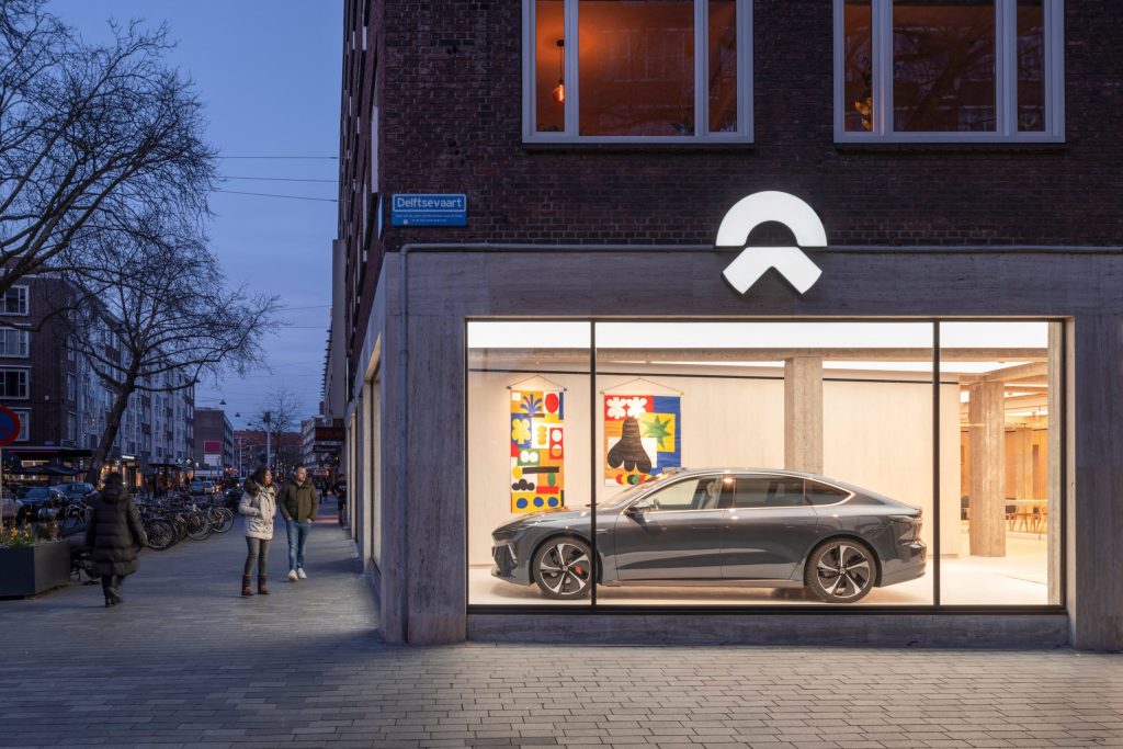 Photograph of NIO House seen through the storefront window, Rotterdam. Design and film by forpeople, courtesy by NIO